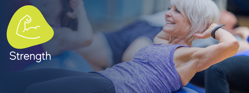 smiling woman performing a sit up on a stability ball with others in the background with an icon indicating its a stability ball strength workout