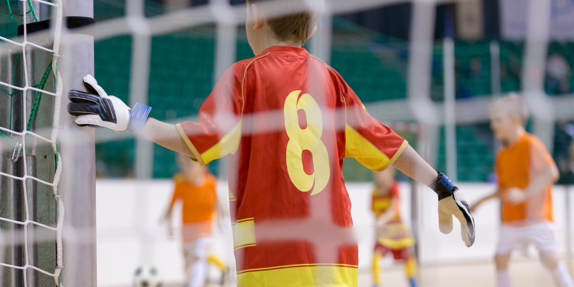 boy standing, holding the goal post awaiting an incoming shot in a futsal game