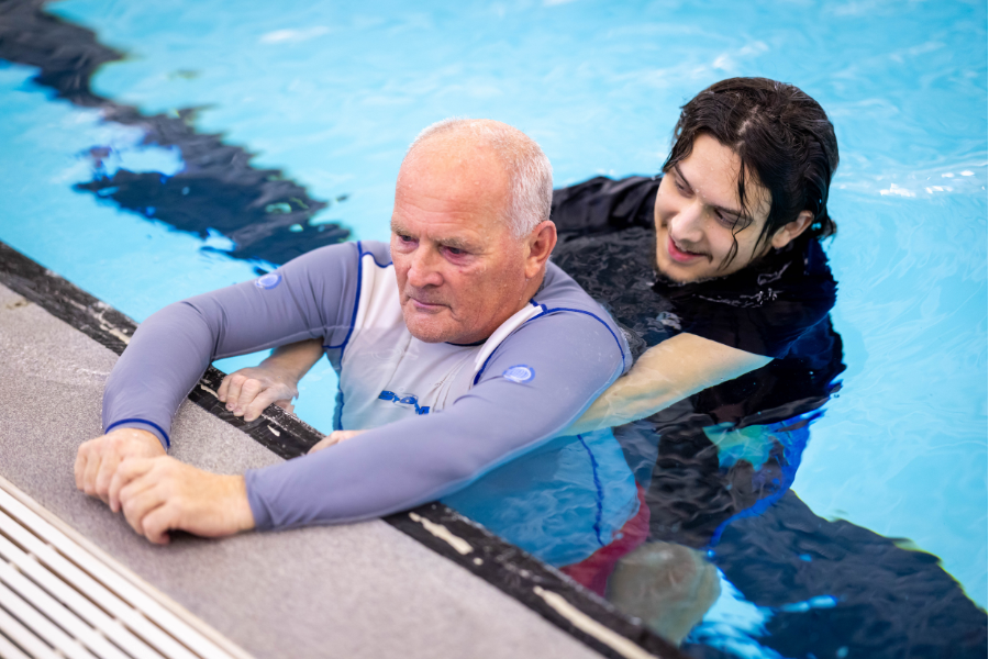 a male lifeguard assisting a male casualty in the support position at the side of the pool in a training session