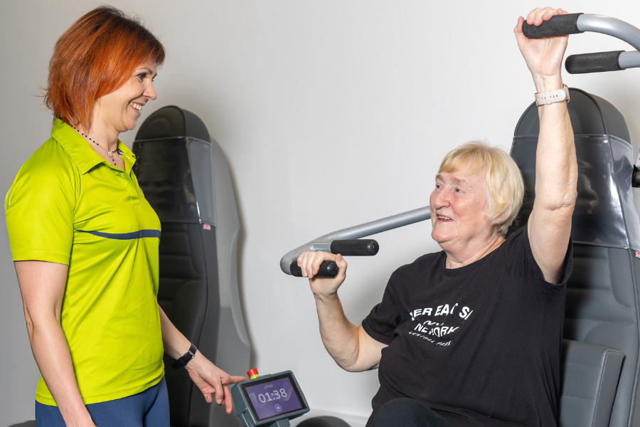 member of staff standing next to a lady on a exercise machine in the active wellbeing suite chatting